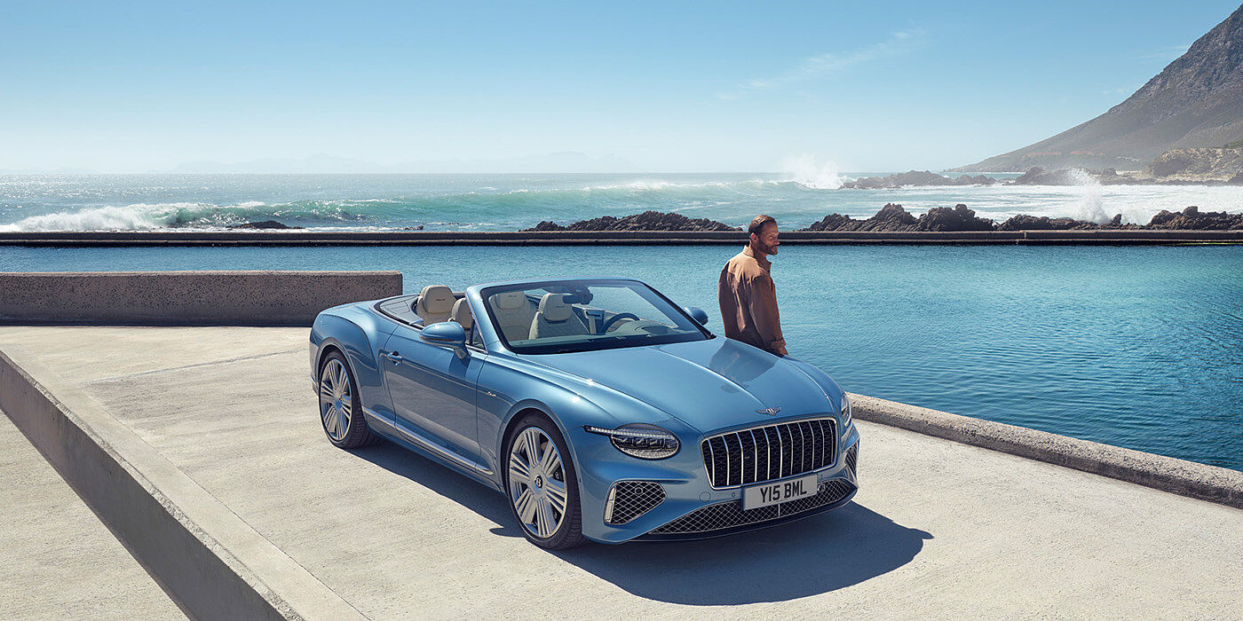 Bentley Warszawa New Bentley Continental GTC Azure convertible front view in Light Windsor blue paint with 22 inch ten spoke wheels parked by the sea in the sunshine