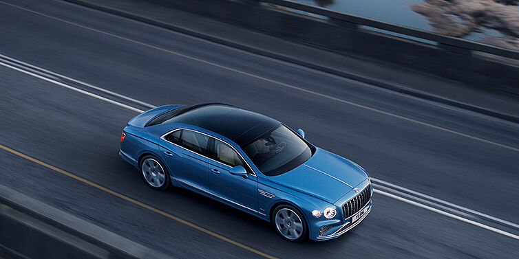 Bentley Warszawa New Bentley Flying Spur Azure sedan in Light windsor blue paint by Mulliner, with 22 inch Azure wheels seen from overhead driving dynamically on a country road