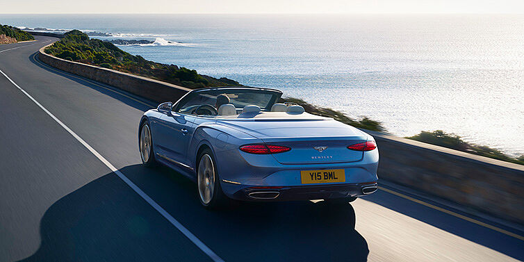 Bentley Warszawa New Bentley Continental GTC Azure convertible rear view in Light Windsor blue paint with 22 inch ten spoke wheels driving dynamically on an ocean road in the sunshine