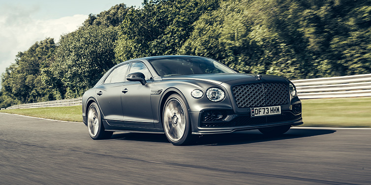 Bentley Warszawa Bentley Flying Spur Mulliner sedan front three quarter in dark grey paint driving dynamically by some trees on a track