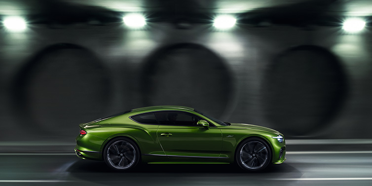 Bentley Warszawa Bentley Continental GT Speed coupe profile in Tourmaline Green driving dynamically past a concrete wall at night