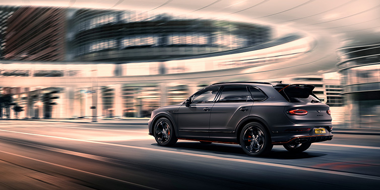 Bentley Warszawa Bentley Bentayga S Black Edition SUV rear three quarter in Anthracite Satin paint driving dynamically through a city at night