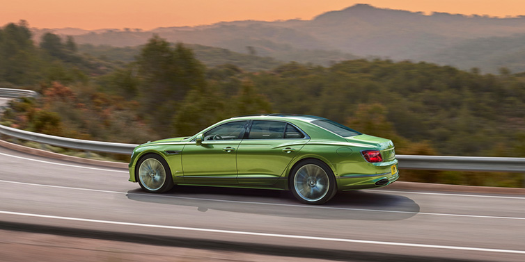 Bentley Warszawa Bentley Flying Spur Speed sedan side profile in Tourmaline Green paint driving dynamically on a mountain road at sunset