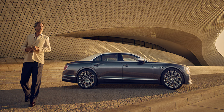 Bentley Warszawa Bentley Flying Spur Mulliner sedan in Rose Gold over Magnetic duotone paint parked by a curved wall with person in suit jacket standing on the left